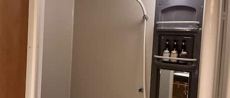 Un baño con bañera, ducha y espejo. Hay botellas en un estante sobre el espejo.