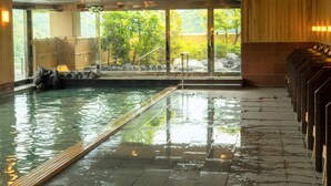 An indoor swimming pool with clear glass walls, a tiled floor, and a view of greenery outside.