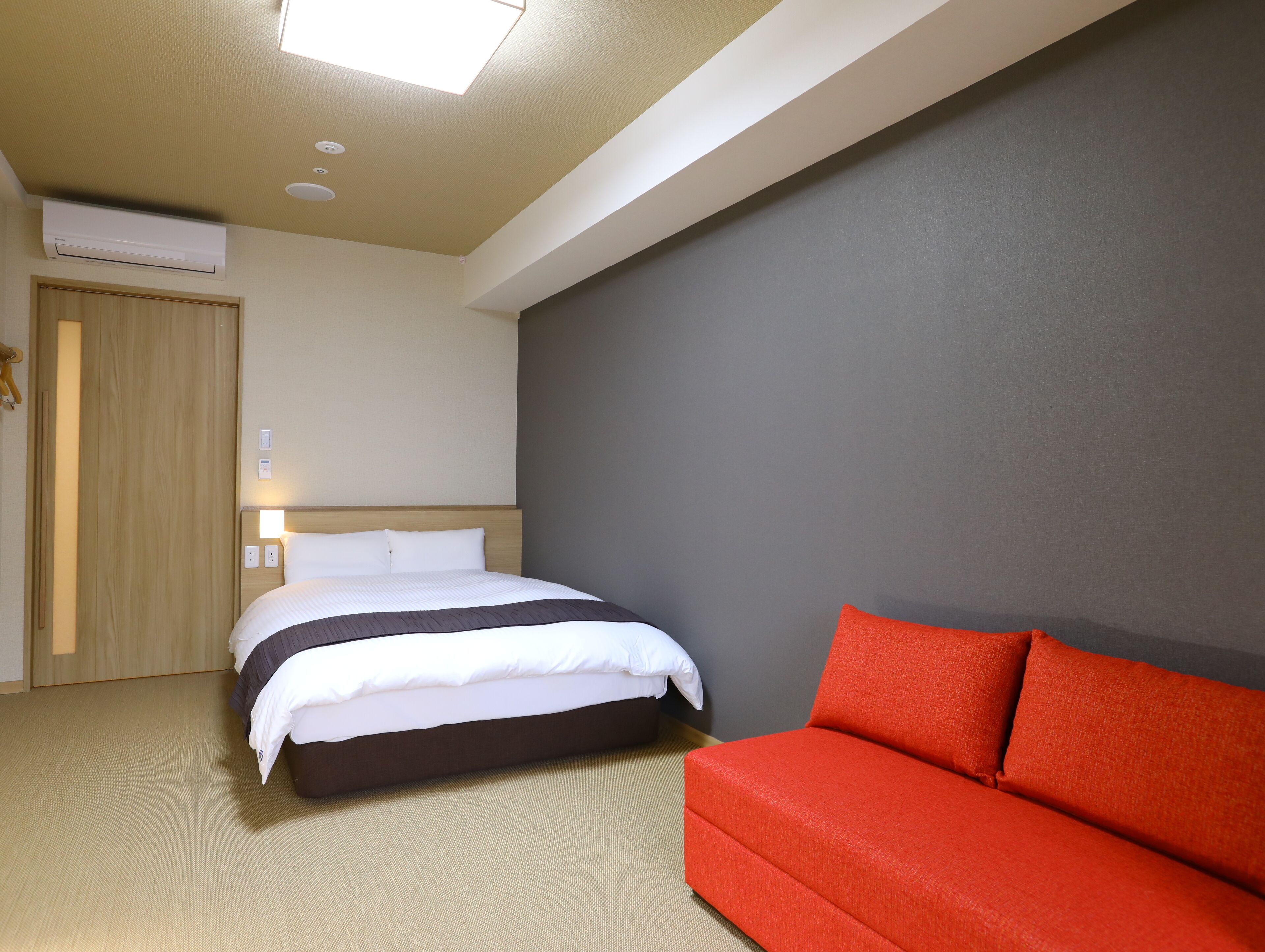 Une chambre d’hôtel avec un lit, un canapé rouge, une armoire en bois et un luminaire au plafond.