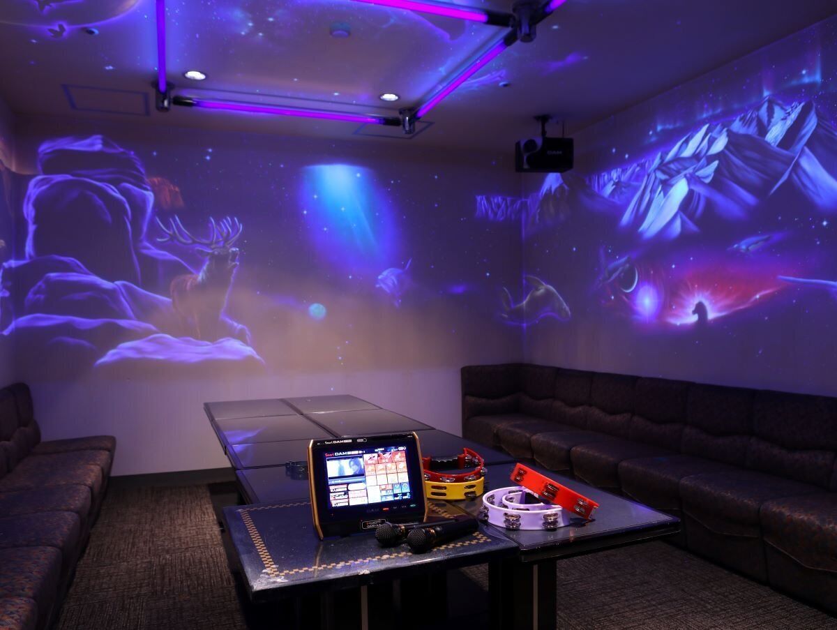 A room with a projection screen displaying a space-themed image, a table with a laptop, a microphone, and some electronic equipment.