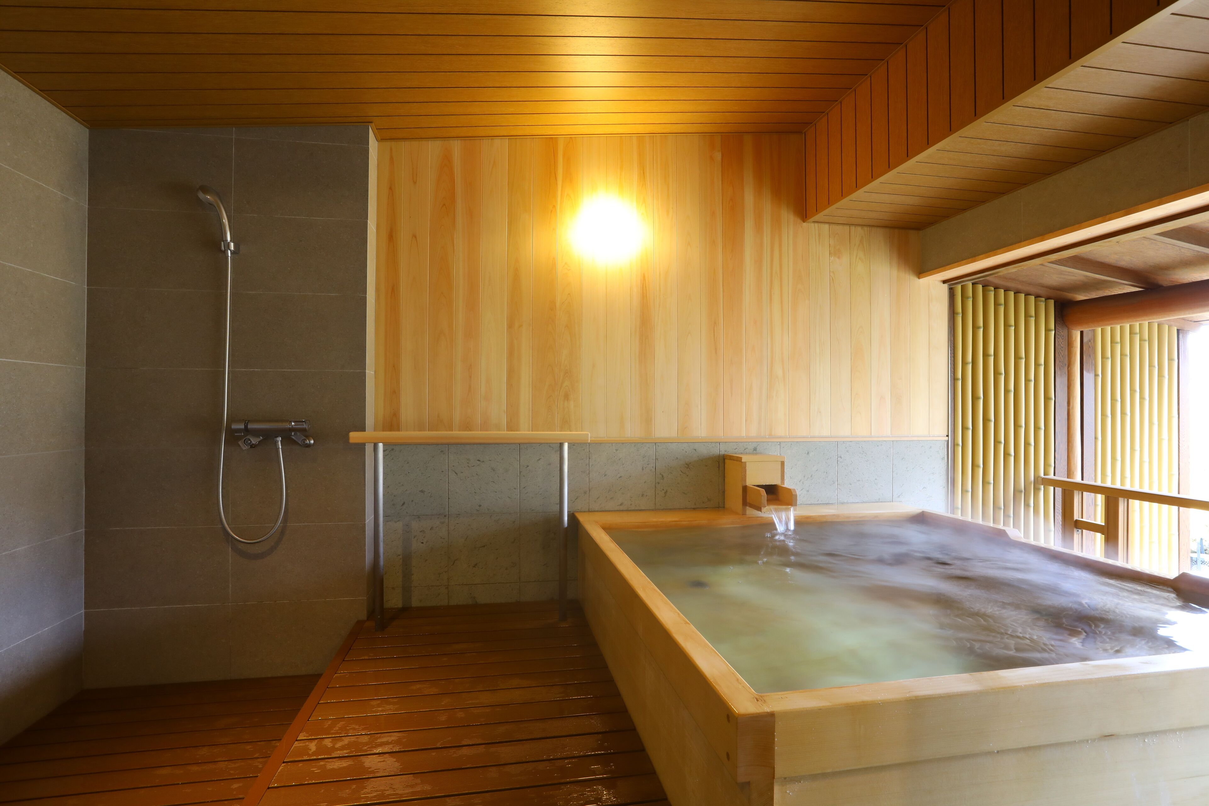 Een houten bad met douche en een houten vloer.