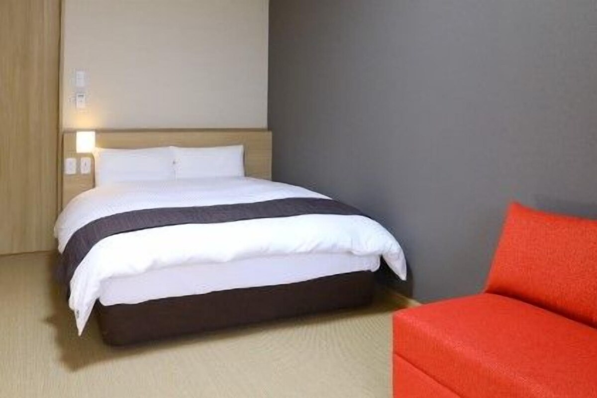 A hotel room with a bed, a red sofa, and a wall-mounted light.