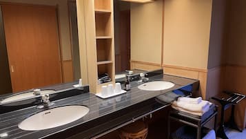 A hotel bathroom with two sinks, a large mirror, and a wooden vanity with shelves.