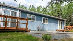 A single-story blue building with a wooden deck, a chair, and a small table. - Alaskan Cozy Home for the Whole Family and Friends (Sterling)