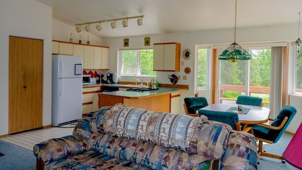 A compact kitchen with a refrigerator, sink, and a dining area with a table and chairs. - Alaskan Cozy Home for the Whole Family and Friends (Sterling)