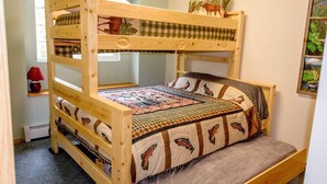 A bunk bed with a quilted bedspread and pillows, a window with a view, and a small table with a lamp. - Alaskan Cozy Home for the Whole Family and Friends (Sterling)