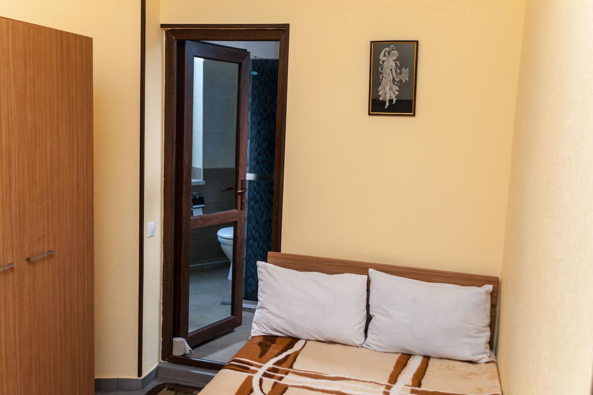 A bedroom with a bed, a wooden wardrobe, and a bathroom visible through an open door.