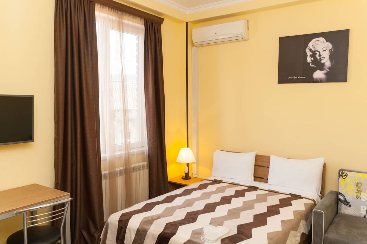 A hotel room with a bed, a desk, a chair, a lamp, and a picture on the wall.