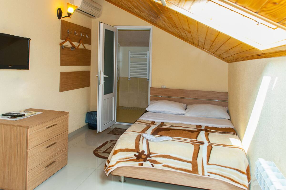 A bedroom with a bed, a wooden dresser, a TV, and a ceiling fan.
