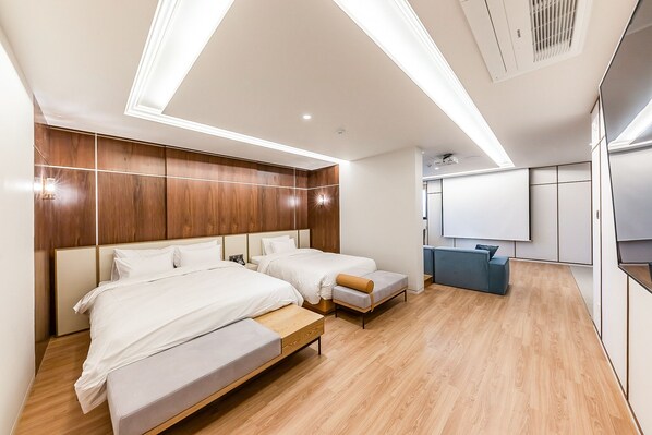 Una habitación de hotel moderna con dos camas, una pequeña zona de estar y una kitchenette.
