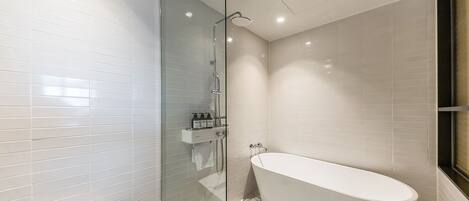 Un baño moderno con ducha envuelta en vidrio, bañera independiente y pared de azulejos blancos.
