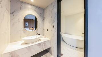 A modern bathroom with a large oval mirror, a white sink, and a freestanding bathtub.
