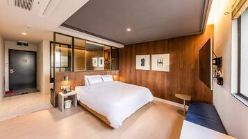 Una habitación de hotel moderna con una cama grande, una mesita de noche, un taburete pequeño, un espejo y obras de arte enmarcadas en la pared.