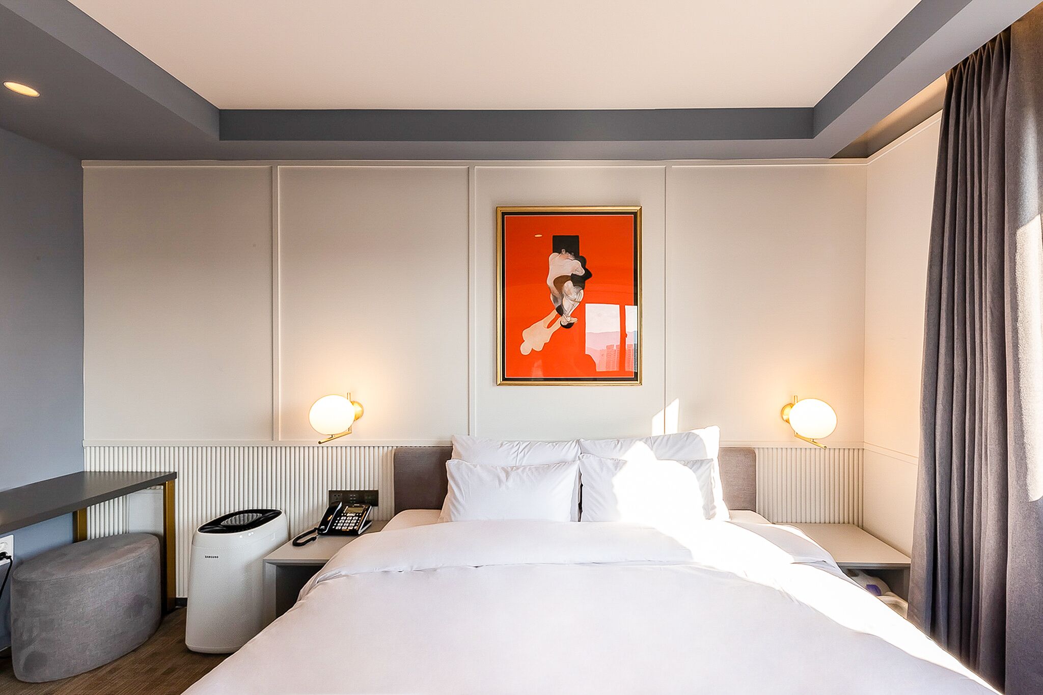 Een hotelkamer met een bed, nachtkastje, lamp en een lijst met kunstwerk aan de muur.