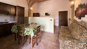 A kitchen with a dining table, chairs, a sofa, and a TV. - Lovely apartment in villa for 2 people with WIFI, pool, TV and patio, close to San Gimignano (Volterra)