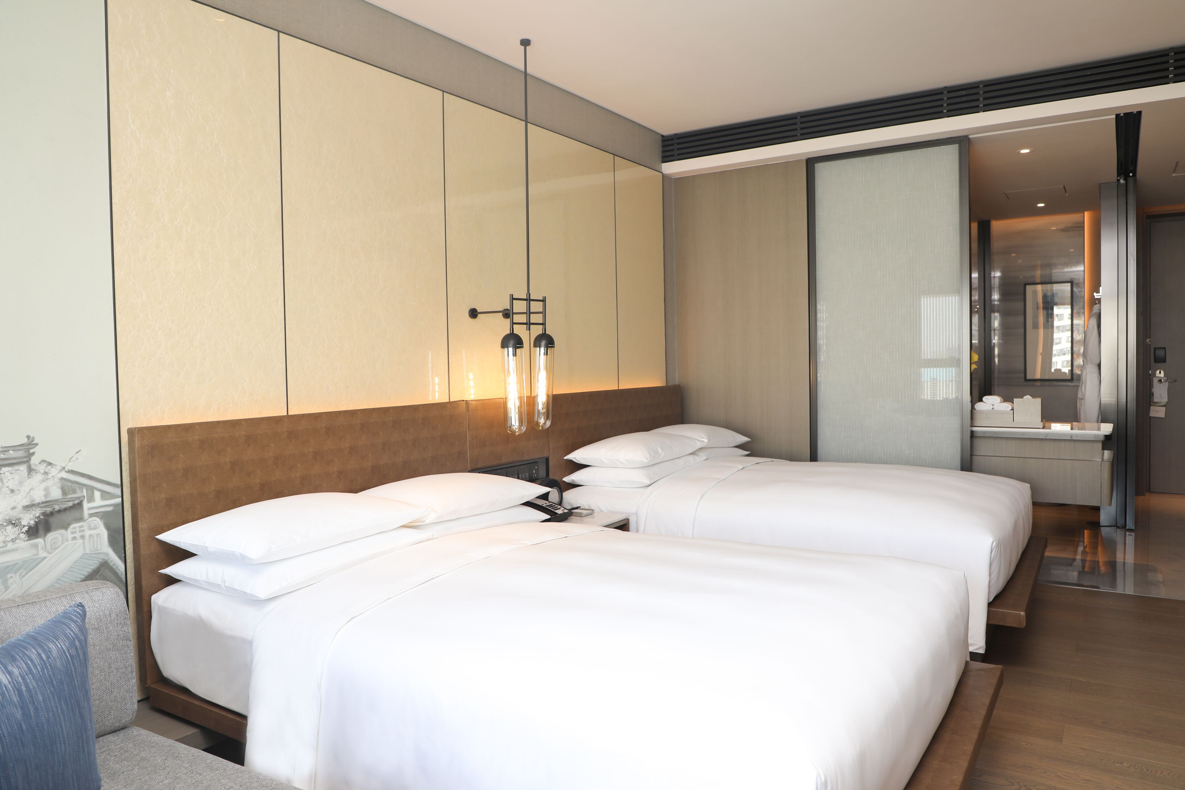 A hotel room with two beds, a wooden headboard, a large mirror, and a modern light fixture.