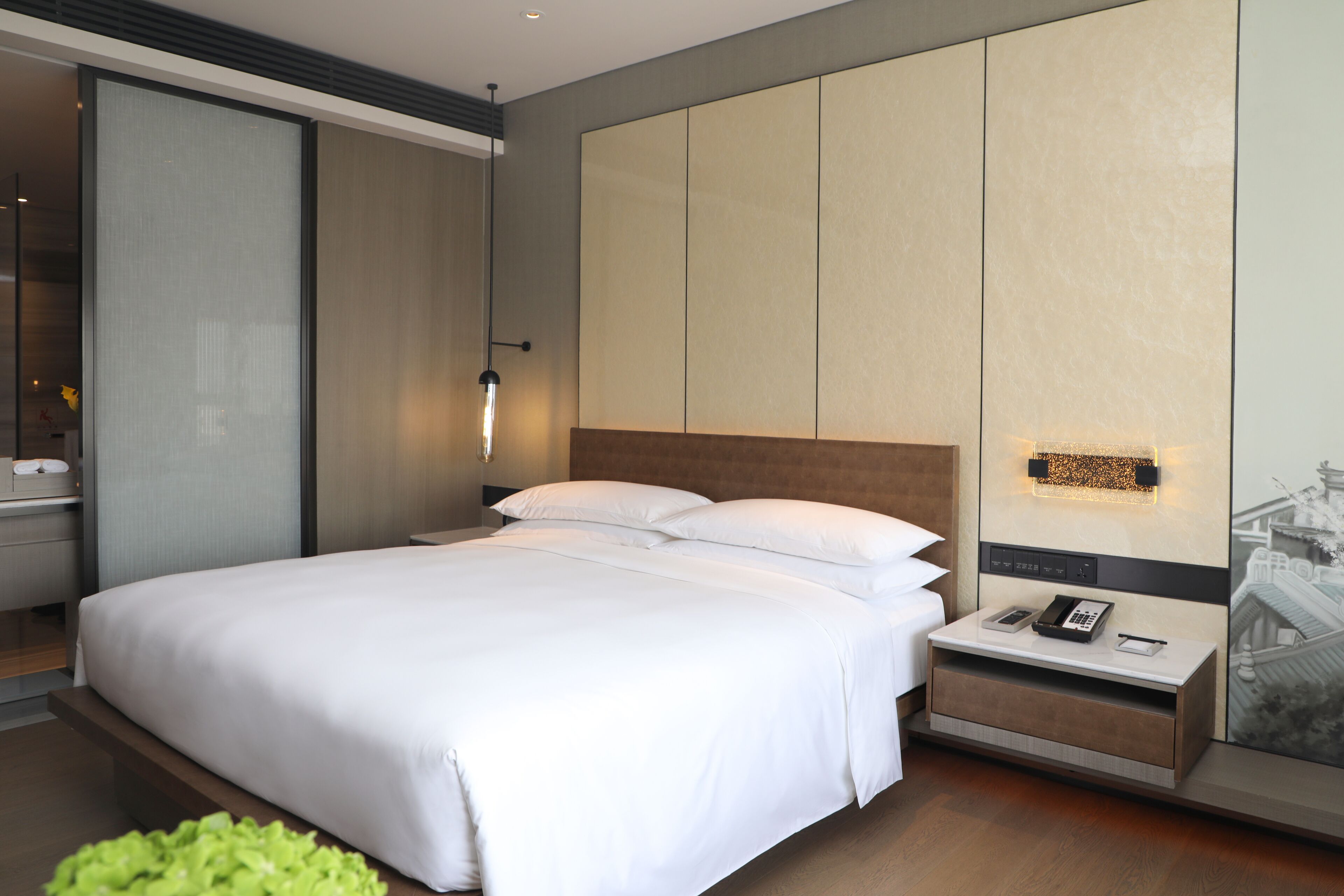 Une chambre d’hôtel moderne avec un grand lit, une table de chevet dotée d’un téléphone et d’une lampe, et une œuvre d’art accrochée au mur.
