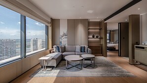 Un salon moderne avec un canapé d’angle, deux tables rondes et une grande fenêtre donnant sur la ville.