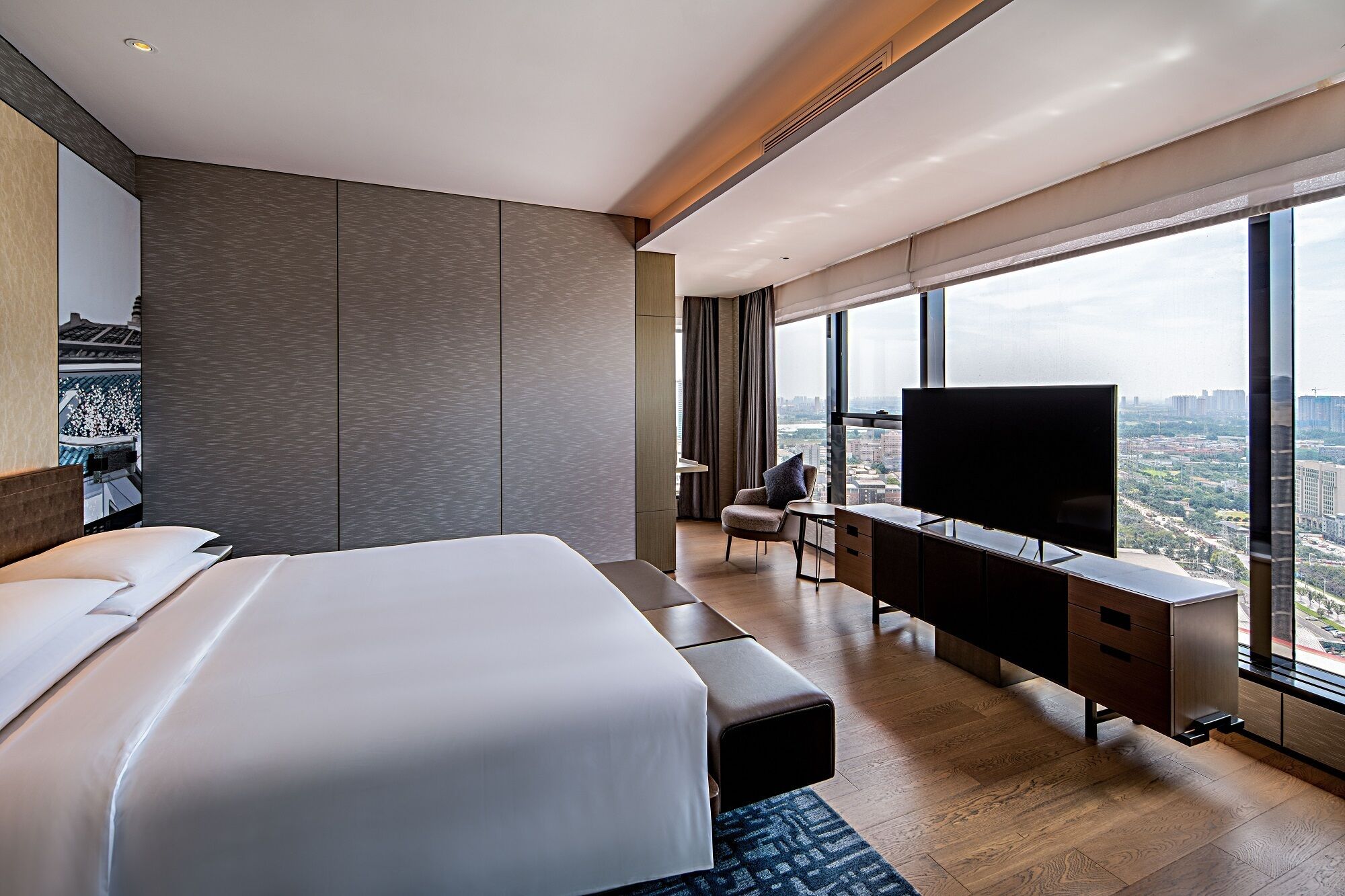 A modern hotel room with a large bed, a desk with a TV, and a city view.