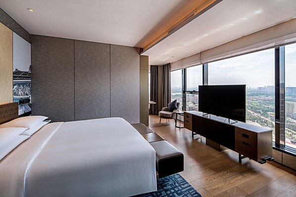 A modern hotel room with a large bed, a desk with a TV, and a city view.