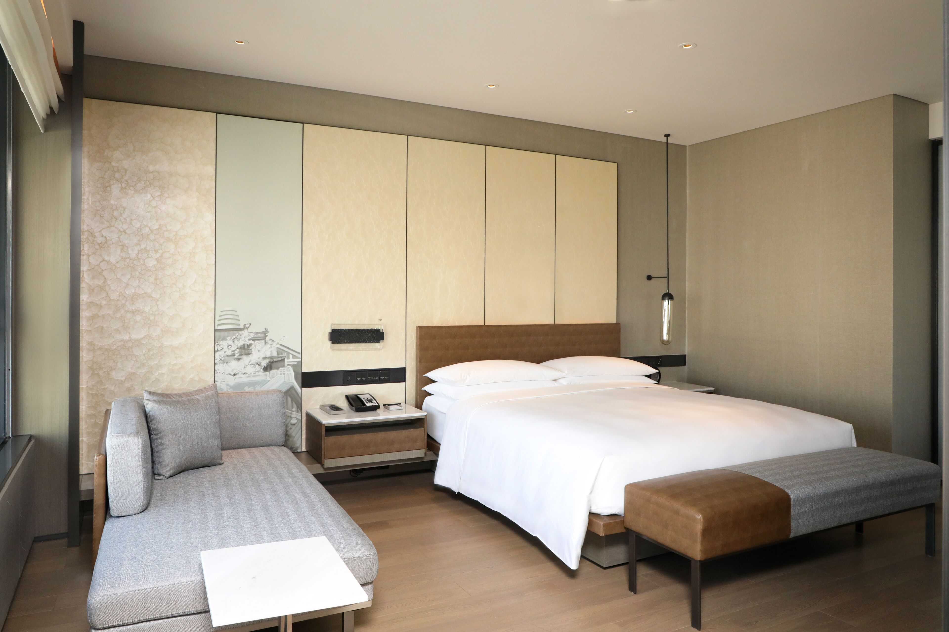 A modern hotel room with a large bed, a sofa, a small table, and a bench.