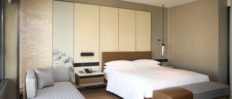 Une chambre d’hôtel moderne avec un grand lit, un canapé, une petite table et un banc.