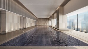 Une piscine intérieure moderne, de forme longue et étroite, dotée de grandes fenêtres sur un côté et offrant une vue sur le paysage urbain.