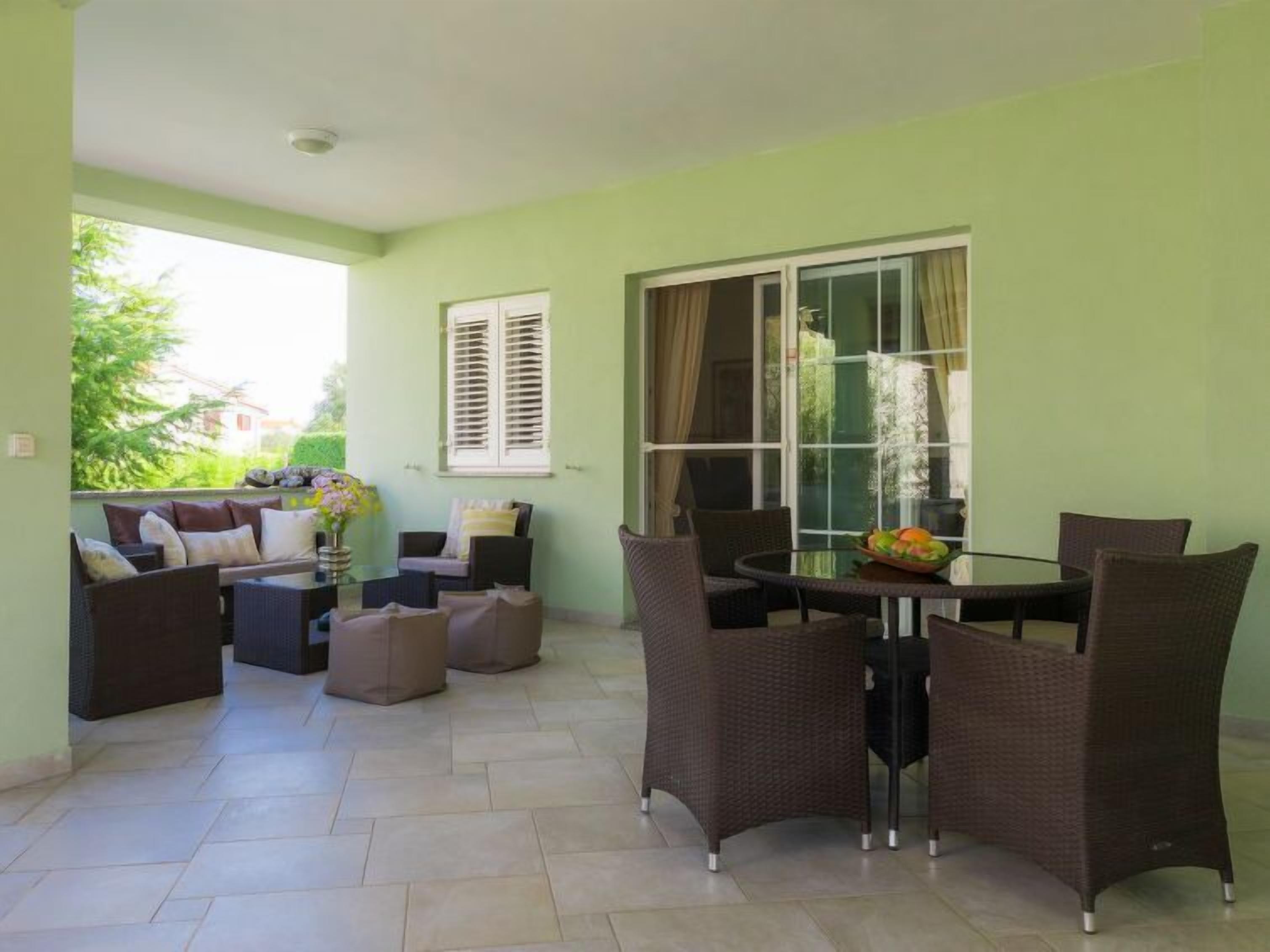 A room with a dining table and chairs, a sofa set, and a window with shutters.