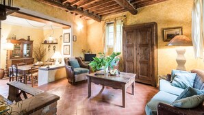 A rustic interior with exposed wooden beams, a dining area with wooden furniture, a living room with a sofa and armchairs, and a large wooden door. - Beautiful private villa for 5 people with WIFI, TV, patio and pets allowed, close to Viareggio (Camaiore)