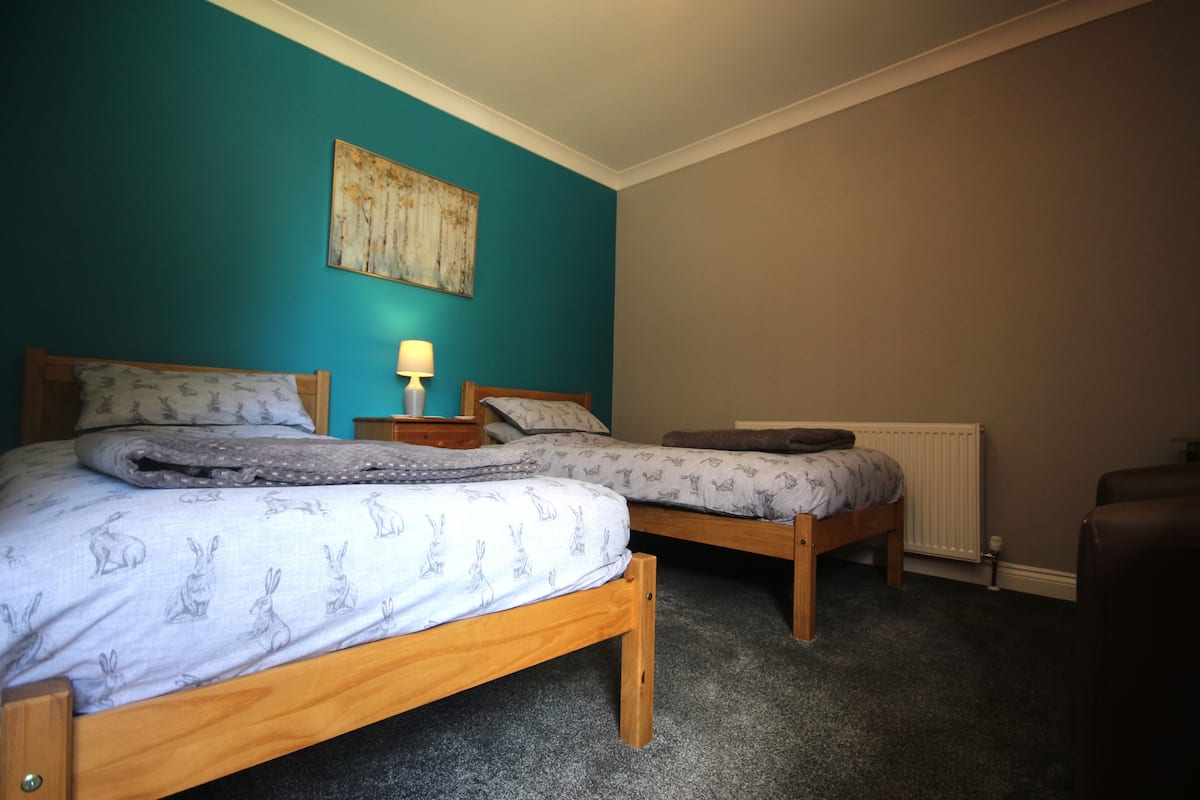 A bedroom with two wooden beds, a nightstand, a lamp, and a radiator.