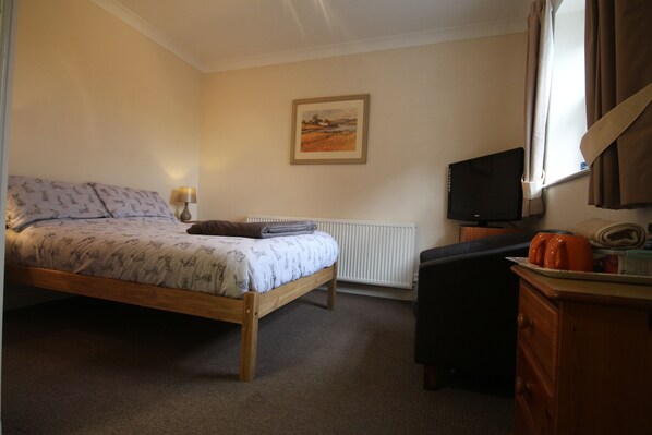 A bedroom with a bed, a desk, a chair, a television, and a radiator.