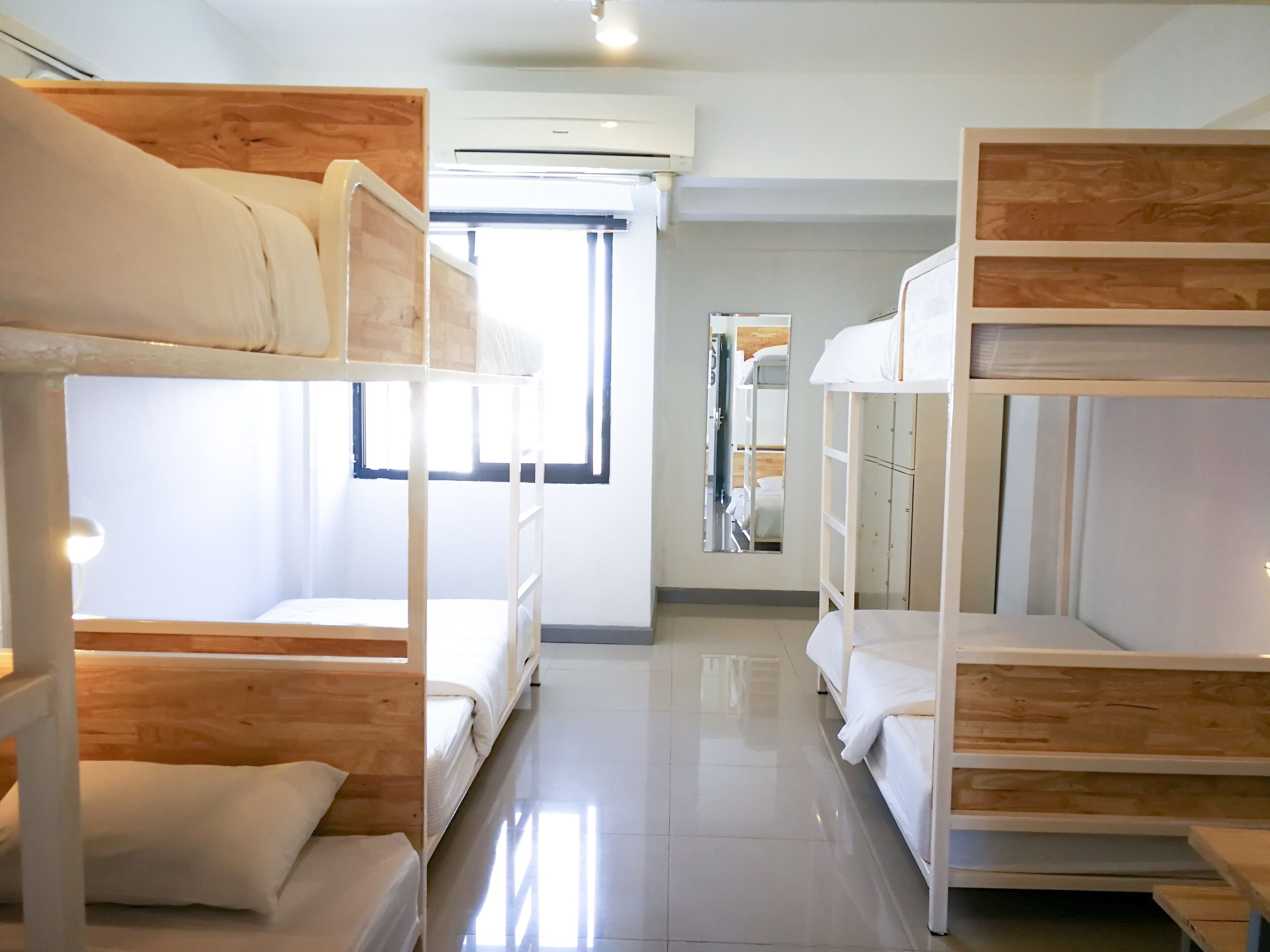 A hotel room with bunk beds, a large mirror, and a window providing natural light.