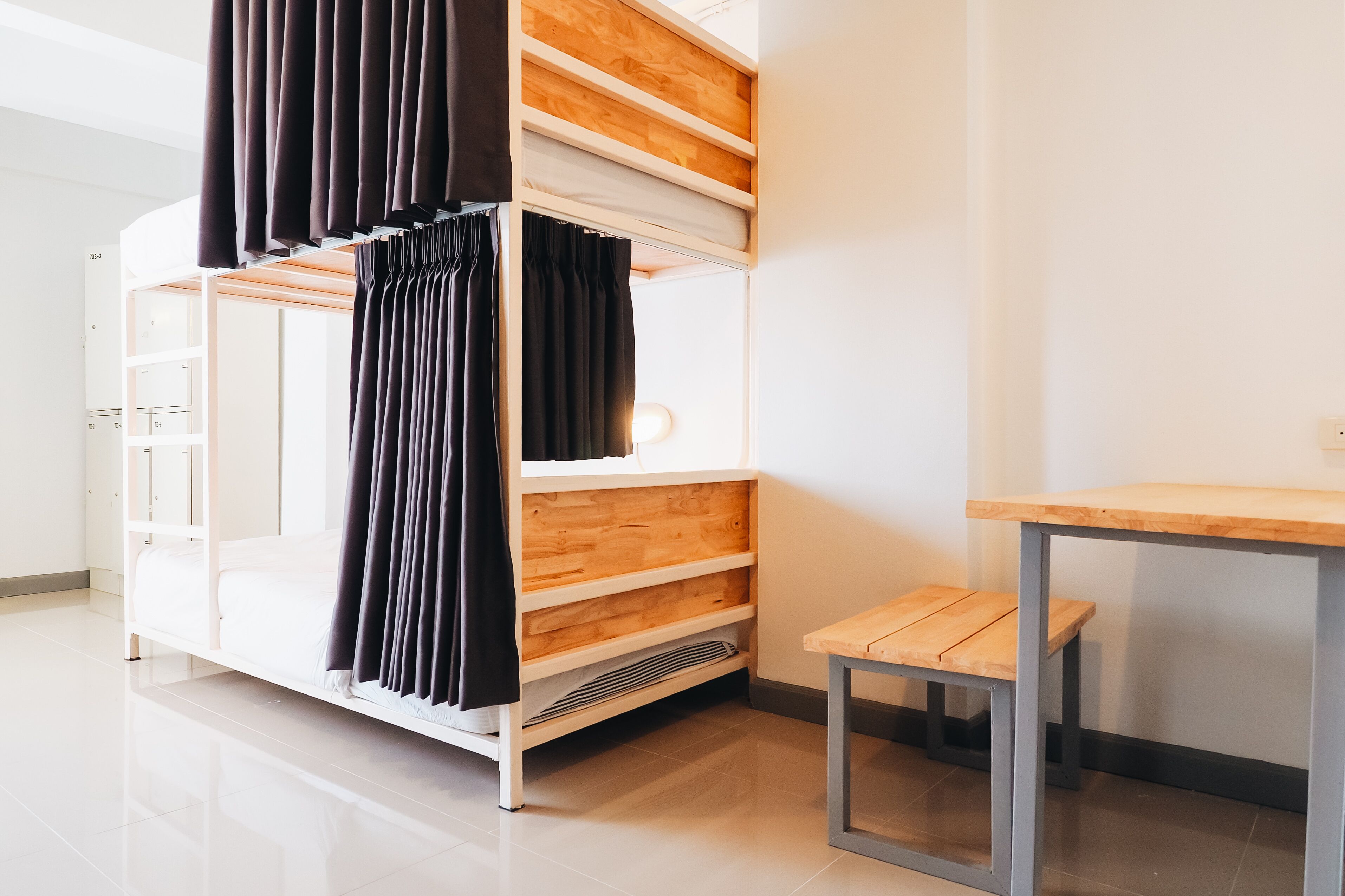 A bunk bed with a wooden frame and black curtains, a small wooden table, and a white wall.