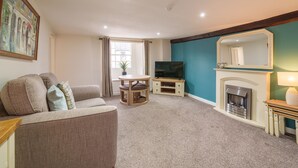 A living room with a sofa, TV, fireplace, and a painting on the wall. - Library View Apartment -  Grade II Listed town centre apartment with parking (Kendal)