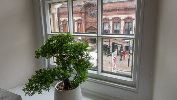 A potted bonsai tree on a windowsill with a view of a red brick building and a pedestrian crossing outside. - Library View Apartment -  Grade II Listed town centre apartment with parking (Kendal)