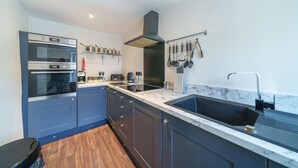 A modern kitchen with dark blue cabinets, a built-in oven, a stainless steel range, a marble countertop, and a hanging utensil rack. - Library View Apartment -  Grade II Listed town centre apartment with parking (Kendal)