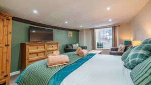 A hotel room with a large bed, a wooden wardrobe, a flat-screen TV, a window with curtains, and a small table with a lamp. - Library View Apartment -  Grade II Listed town centre apartment with parking (Kendal)