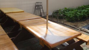 Ein langer Holztisch mit Bänken, ein Metallhocker und ein kleiner Gartenbereich mit Pflanzen.