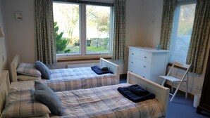 A bedroom with two beds, a dresser, and a chair. - Calluna Cottage -  a cottage that sleeps 7 guests  in 3 bedrooms (Dalbeattie)