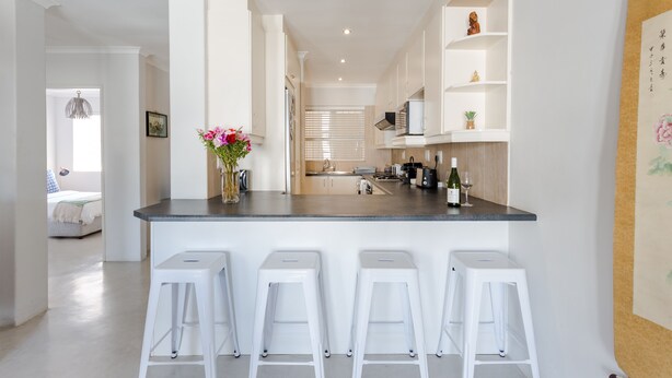 A modern kitchen with a central island, white bar stools, and a decorative vase with flowers. - 211 De Waterkant Piazza (Cape Town)