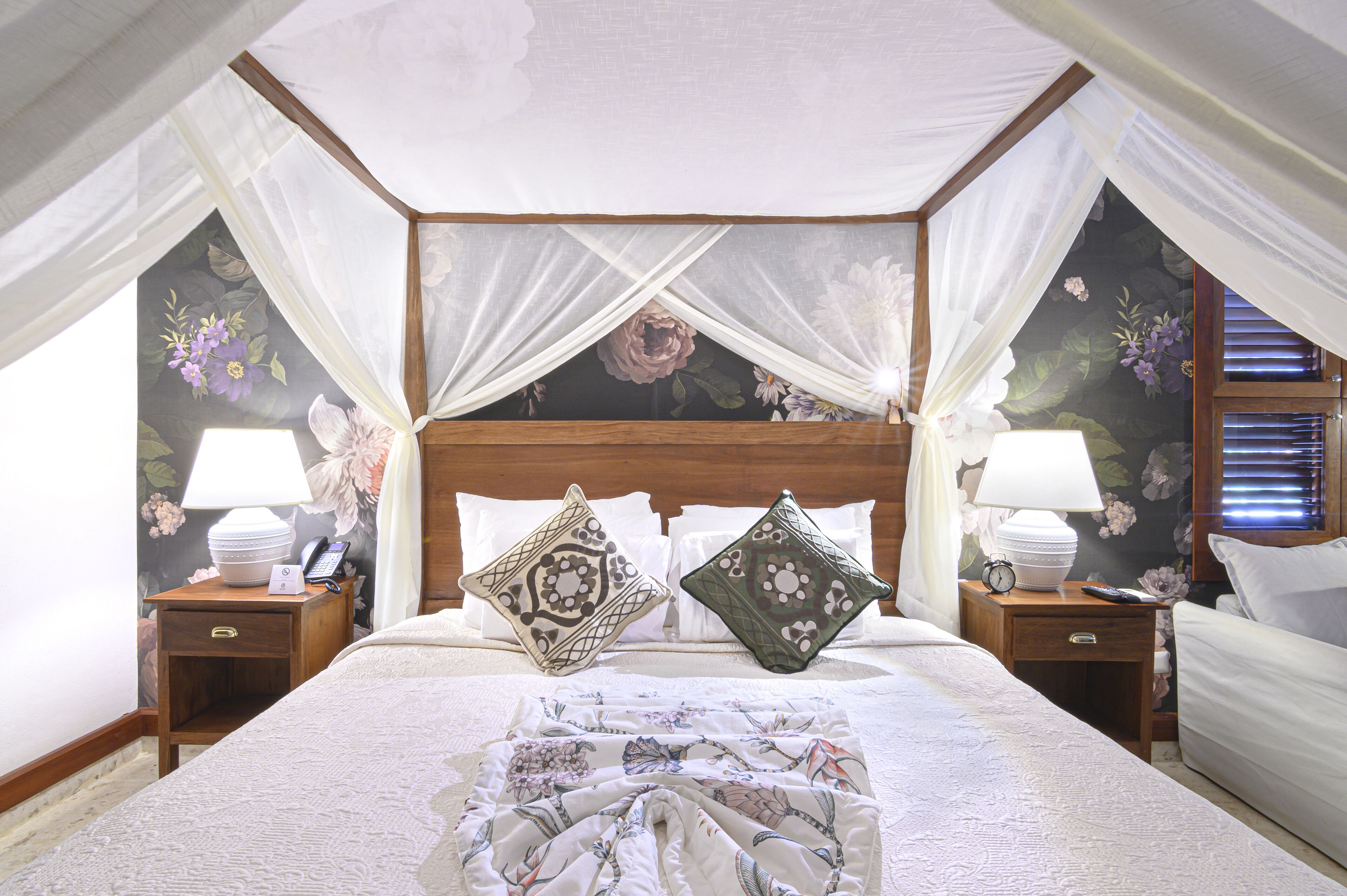 Una cama con dosel adornada con papel tapiz floral y dos mesitas de noche con lámparas.
