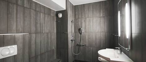 Un baño moderno con ducha a ras de suelo, tocador con espejo y lámpara de pared.