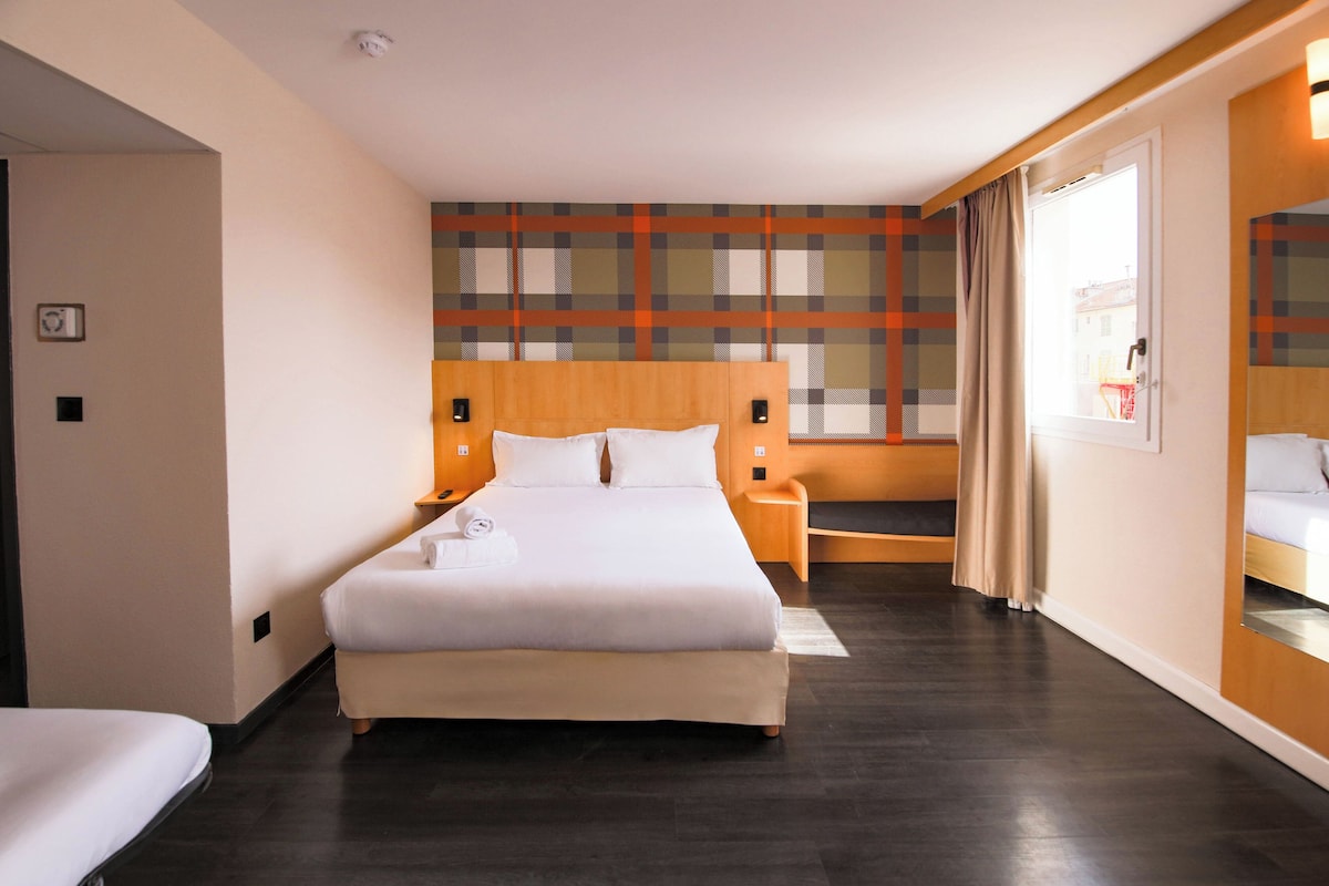 A hotel room with a large bed, bedside tables, a small seating area, and a window with curtains.