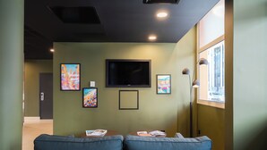 A waiting area with a flat-screen TV mounted on the wall, two blue cushioned seating areas, and framed artworks on the walls. -  easyHotel Nice Old Town (Nice)