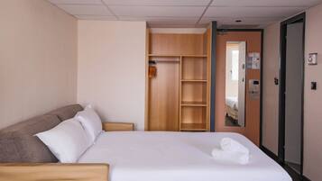 A hotel room with a bed, a wooden wardrobe, a mirror, and a door with a control panel.
