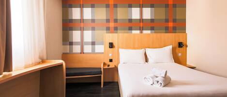 A hotel room with a bed, a bench, a nightstand, and a wall with a plaid pattern.