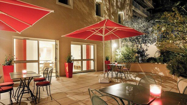 An outdoor patio area with tables and chairs, red umbrellas, and potted plants. -  easyHotel Nice Old Town (Nice)