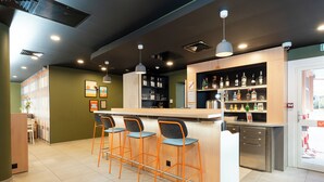 A modern bar area with a wooden counter, three bar stools, and shelves stocked with bottles. -  easyHotel Nice Old Town (Nice)