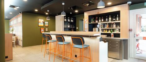 A modern bar area with a wooden counter, three bar stools, and shelves stocked with bottles.