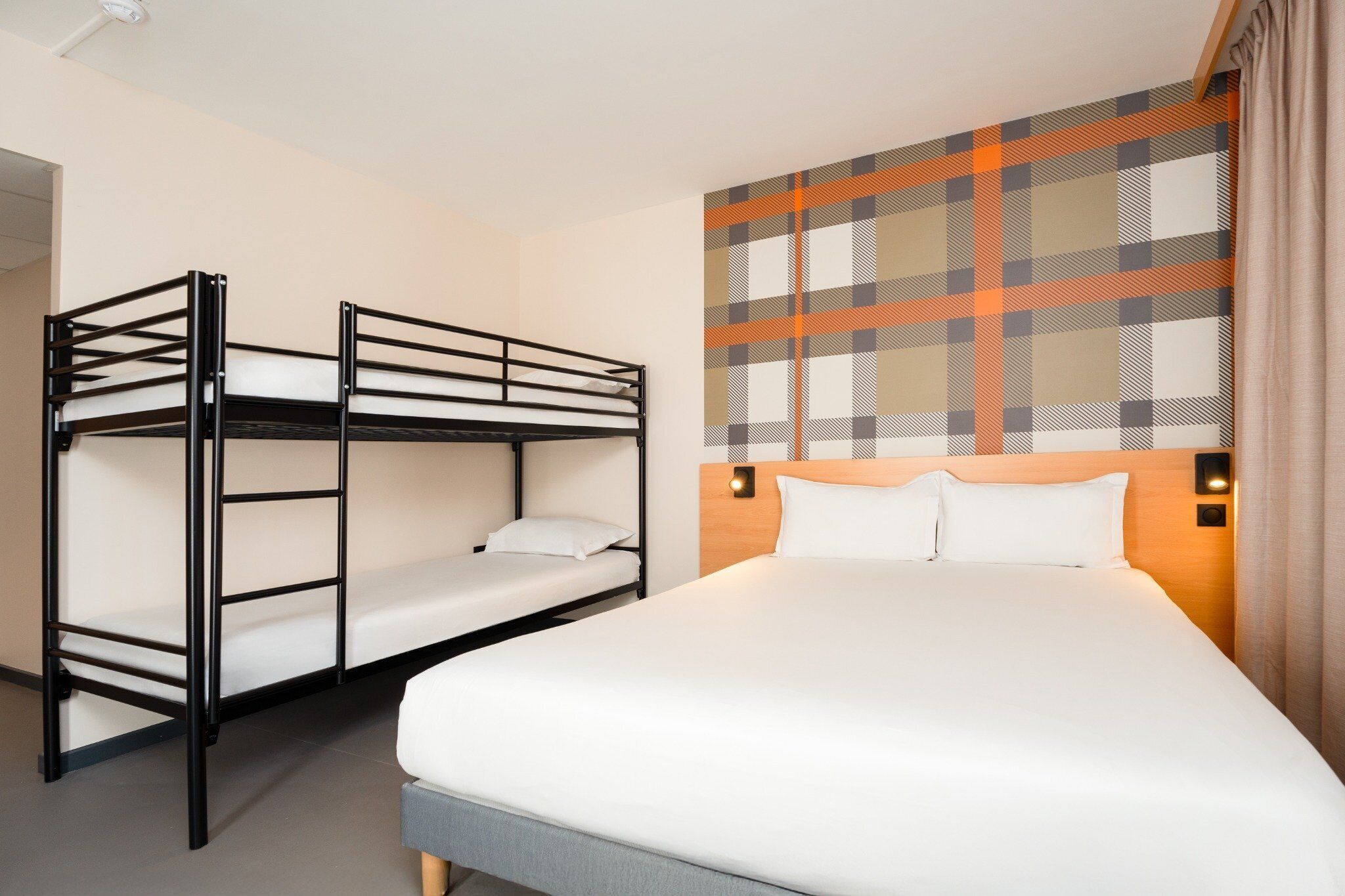 Habitación de hotel con literas, una cama individual y una pared con estampado escocés.